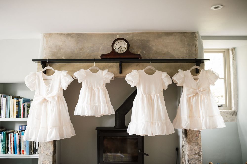 A row of vintage white dresses and lace garments hanging on display against a white wall in soft lighting.