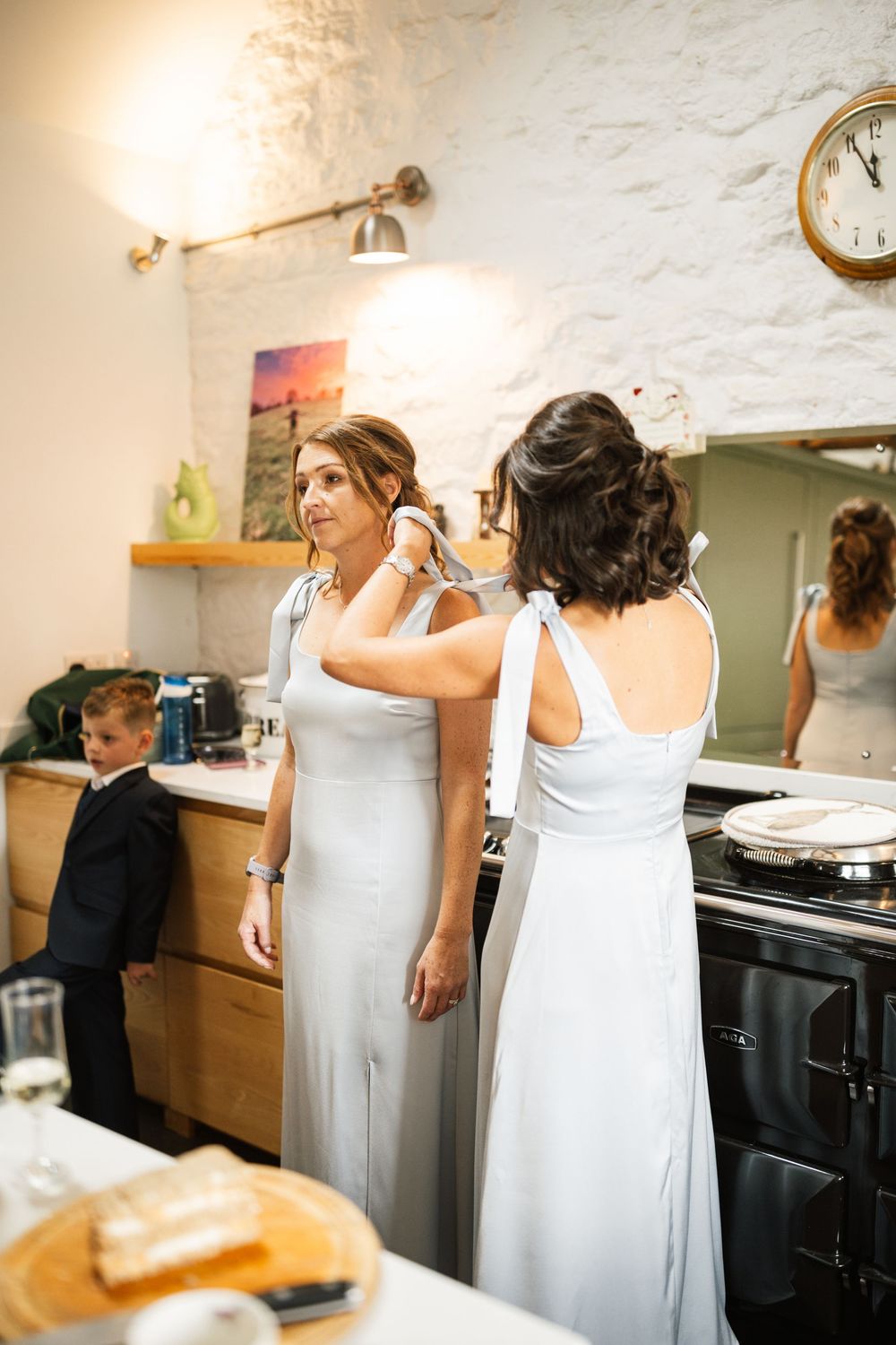 Women in white dresses preparing in a rustic room with stone walls and vintage decor.