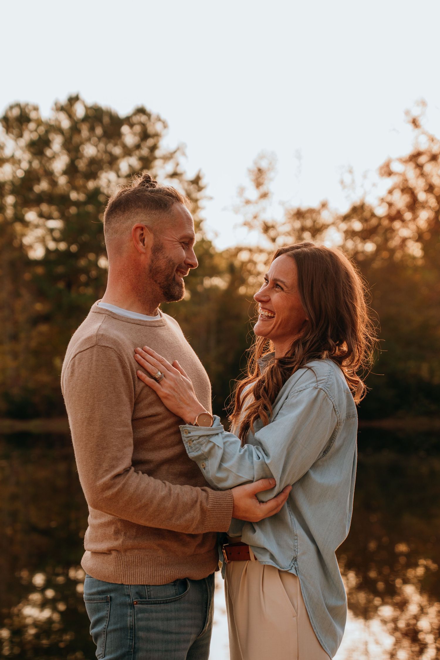 Family stands together in a golden field at sunset with trees in the background.