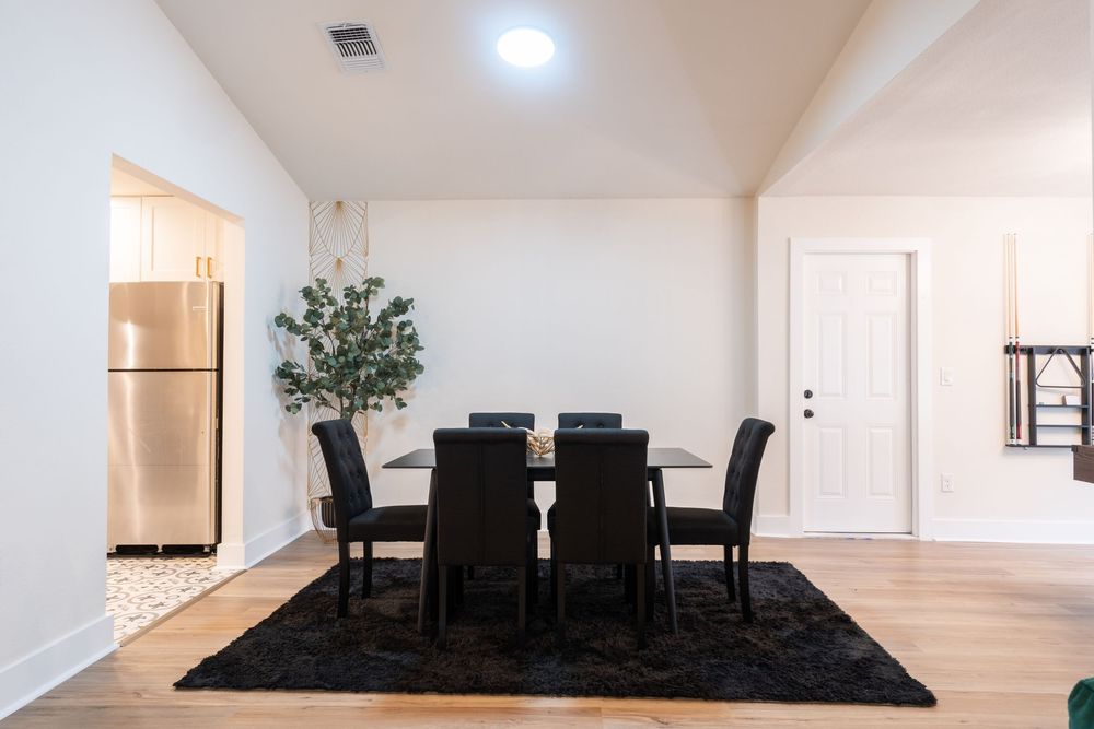Modern dining room with black chairs and table on dark rug with minimalist decor.