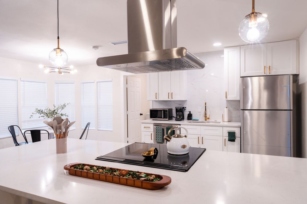 Contemporary white kitchen with stainless steel appliances, pendant lights, and sleek cabinetry.