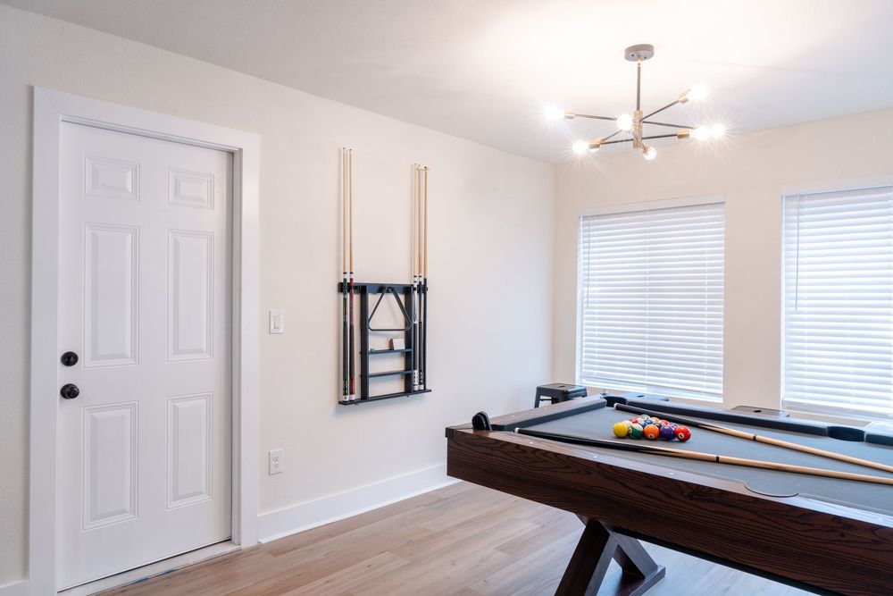 Game room with pool table, white walls and modern ceiling light fixture.