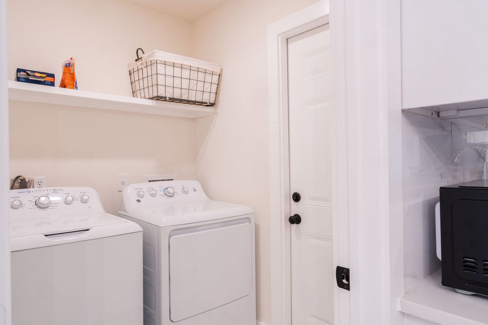 Modern white laundry room with washer, dryer, and storage cabinets featuring clean lines and bright lighting.