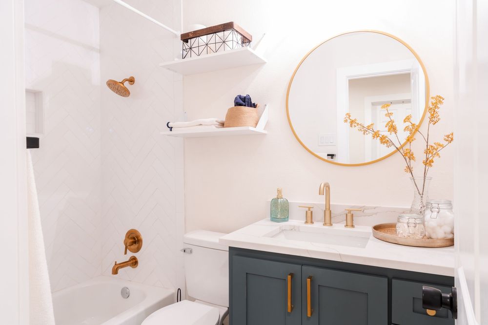 Modern bathroom with gold accents, teal vanity, and round mirror.