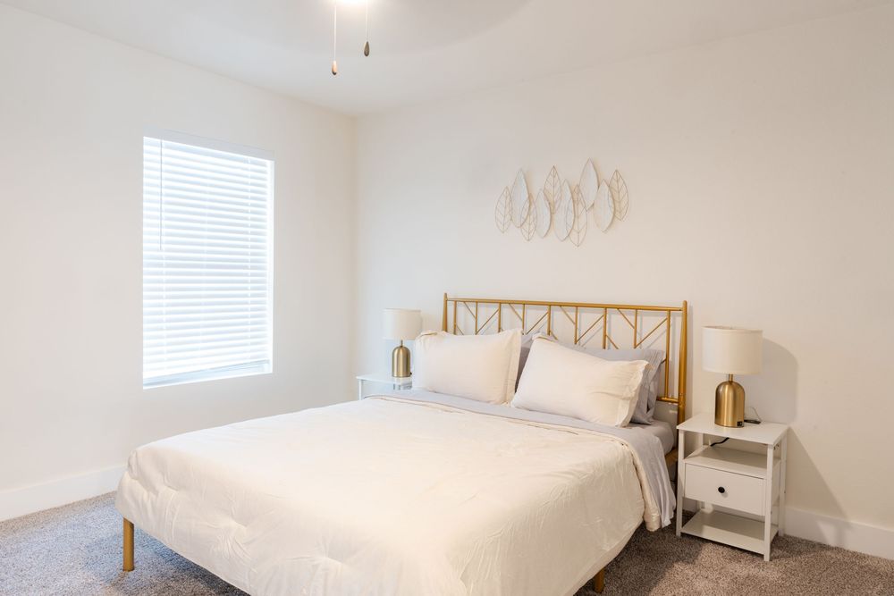 Spacious bedroom featuring white bedding, wooden headboard, and bedside tables with lamps.