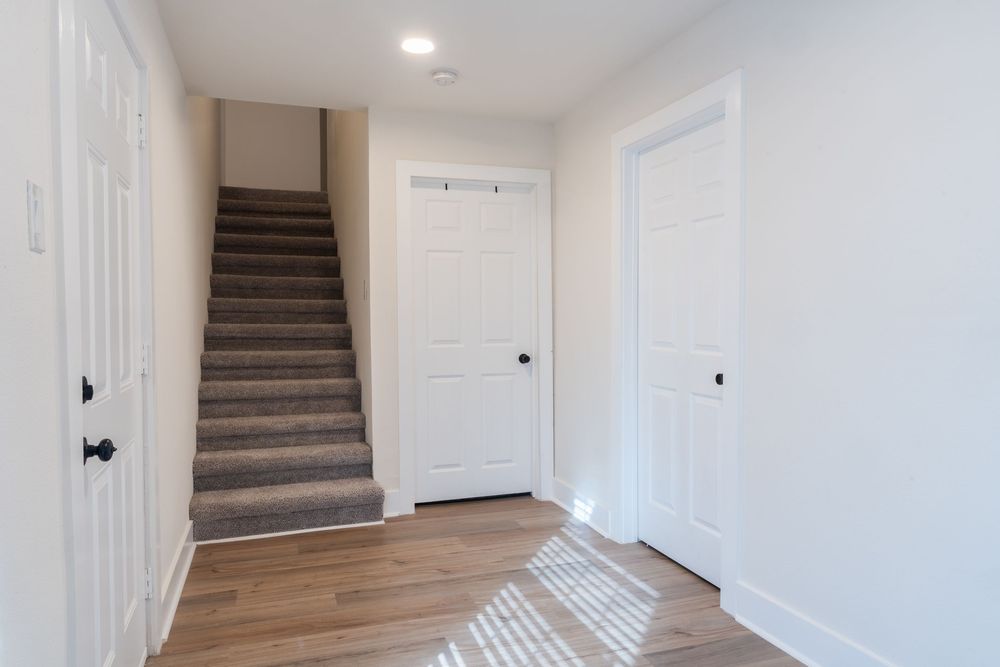 White hallway with wooden flooring and carpeted stairs leading to upper level.