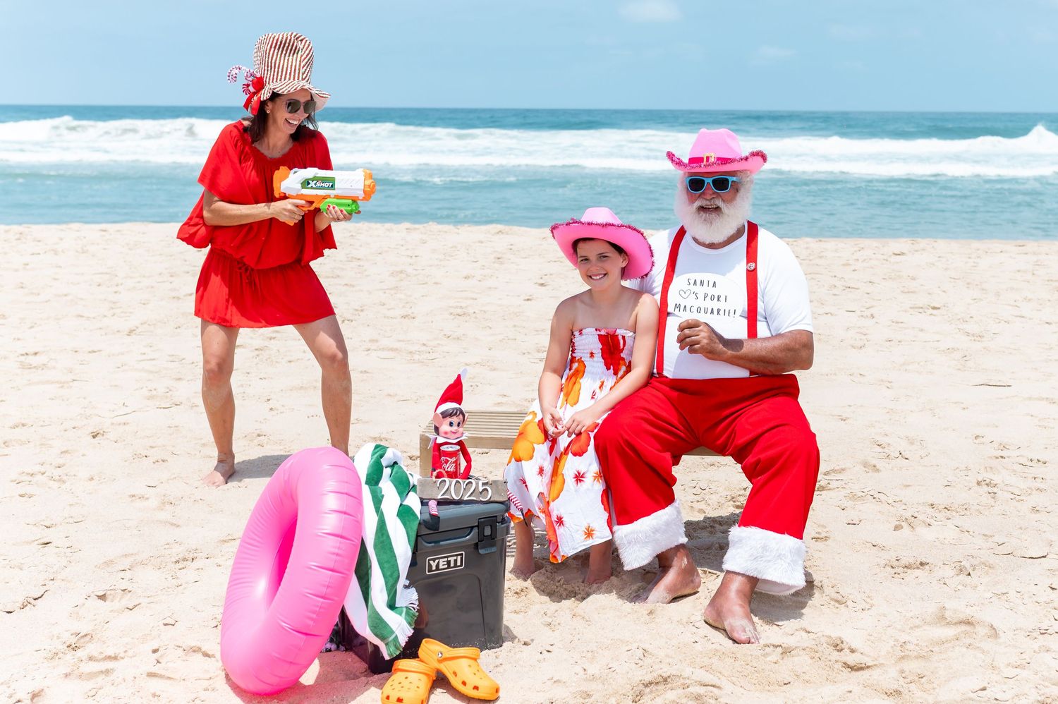 Festive holiday scene on a beach with red and white decorations, a bicycle, and coastal views in the background.