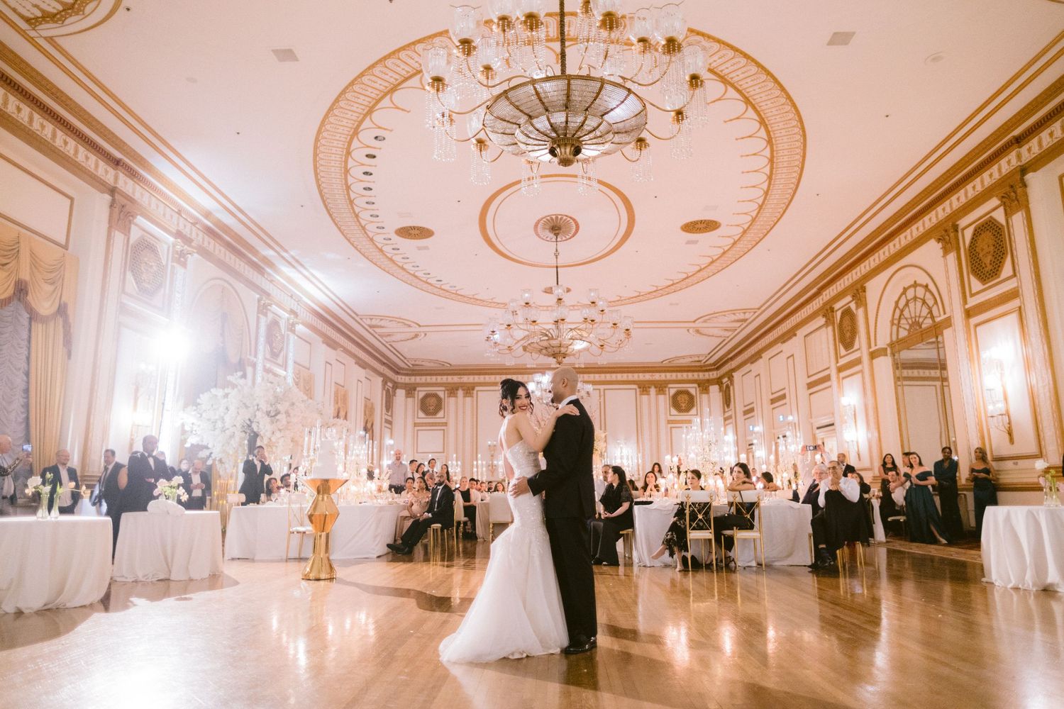 A panoramic view of an elegant ballroom with ornate chandeliers, decorative ceiling details and classic white decor.