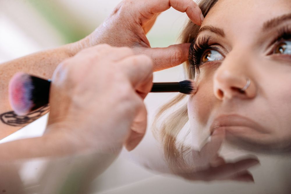 Professional makeup artist applying mascara to client's eyelashes during beauty treatment session.