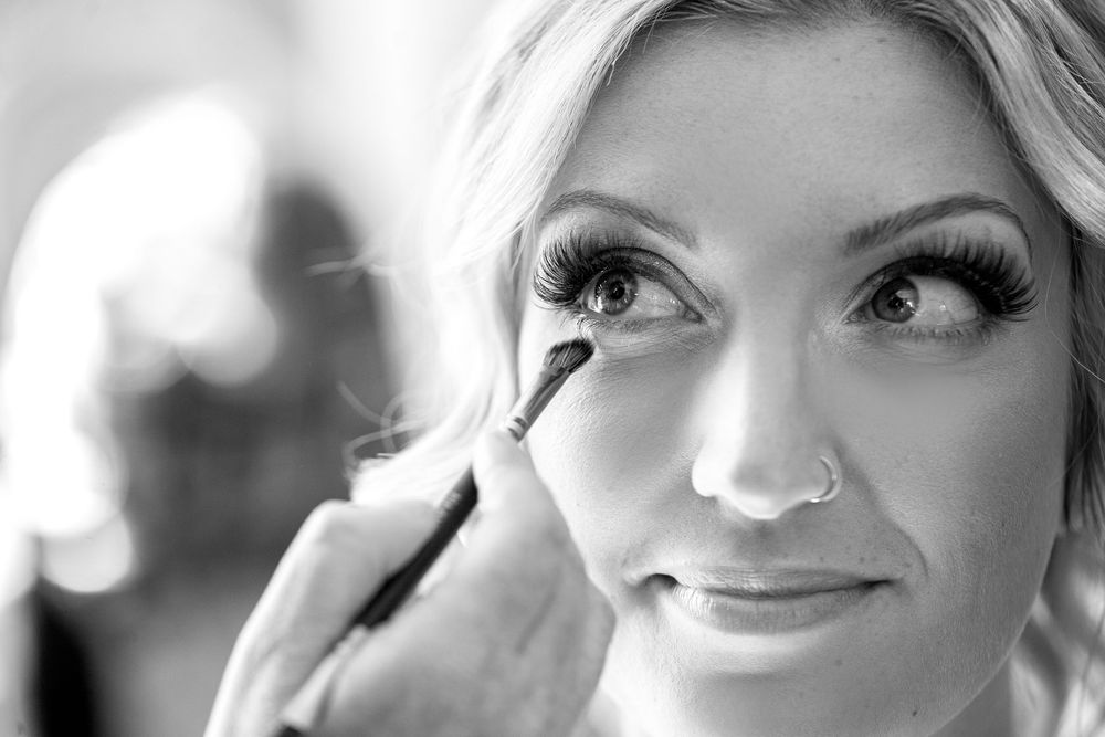 Black and white portrait photograph showing a person with long eyelashes and a slight smile looking to the side.