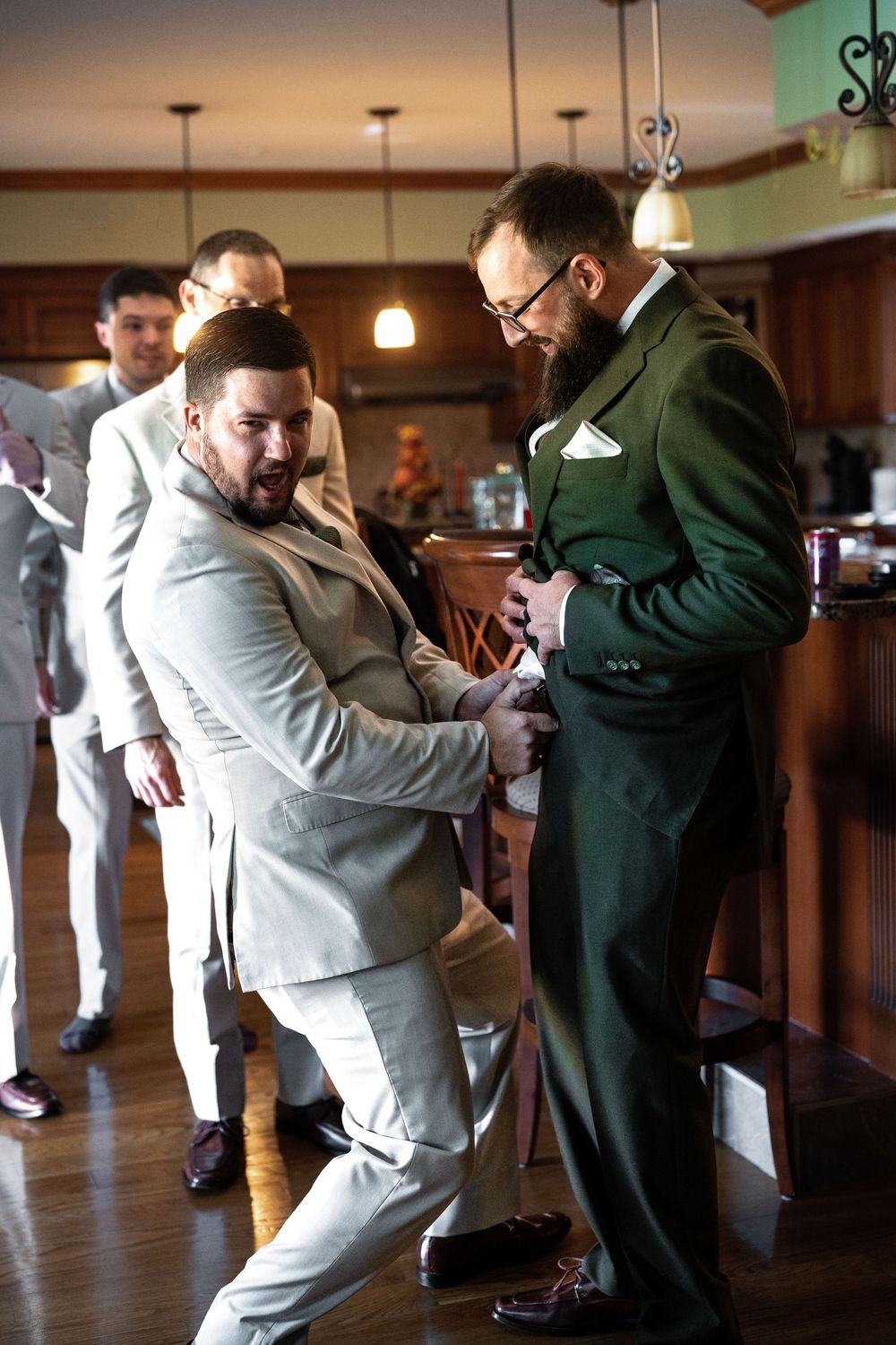 Two people in formal attire share a lighthearted moment on a wooden dance floor under pendant lights at an indoor venue.