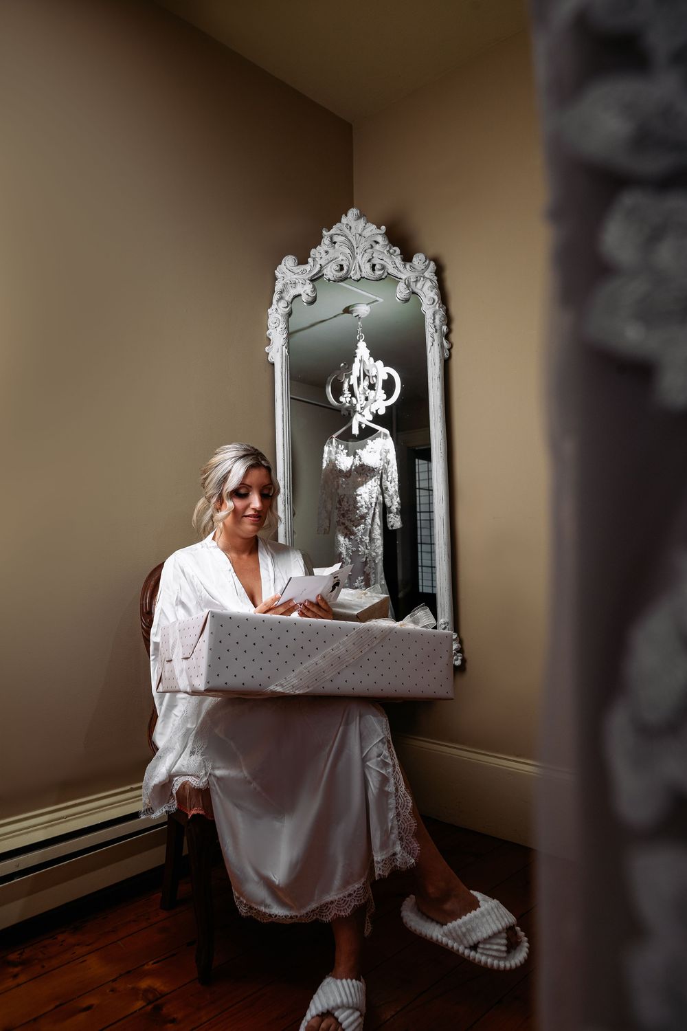 A person in white sits at a vintage vanity mirror in a dimly lit room with warm lighting.