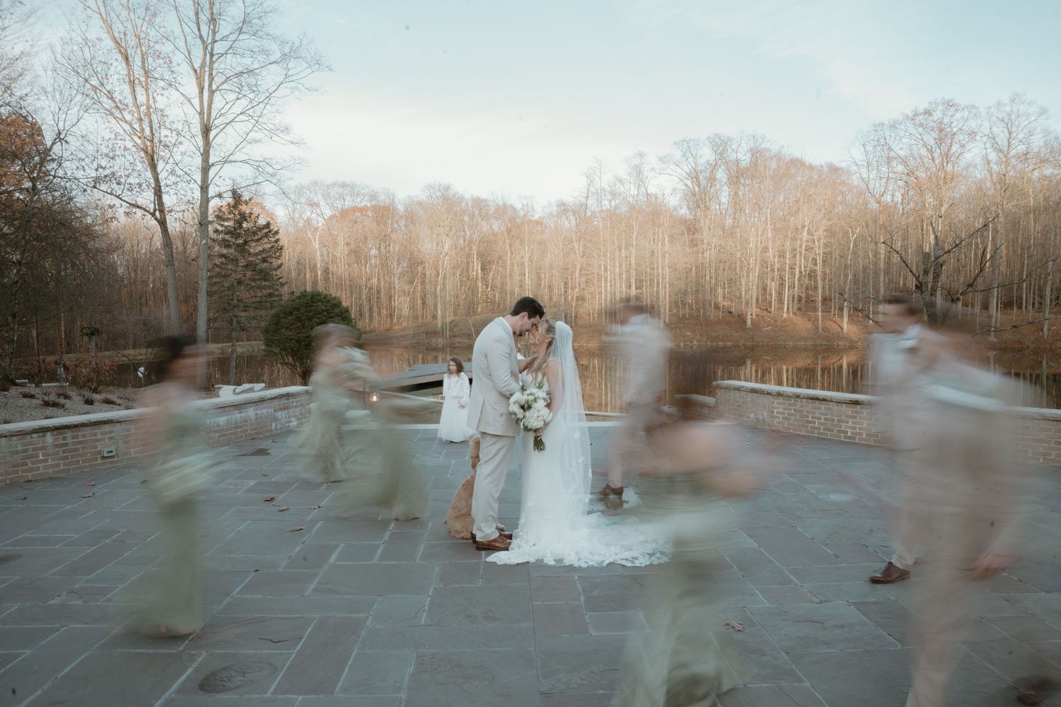 Large wedding party in blue bridesmaid dresses and gray suits celebrating outdoors in a field.