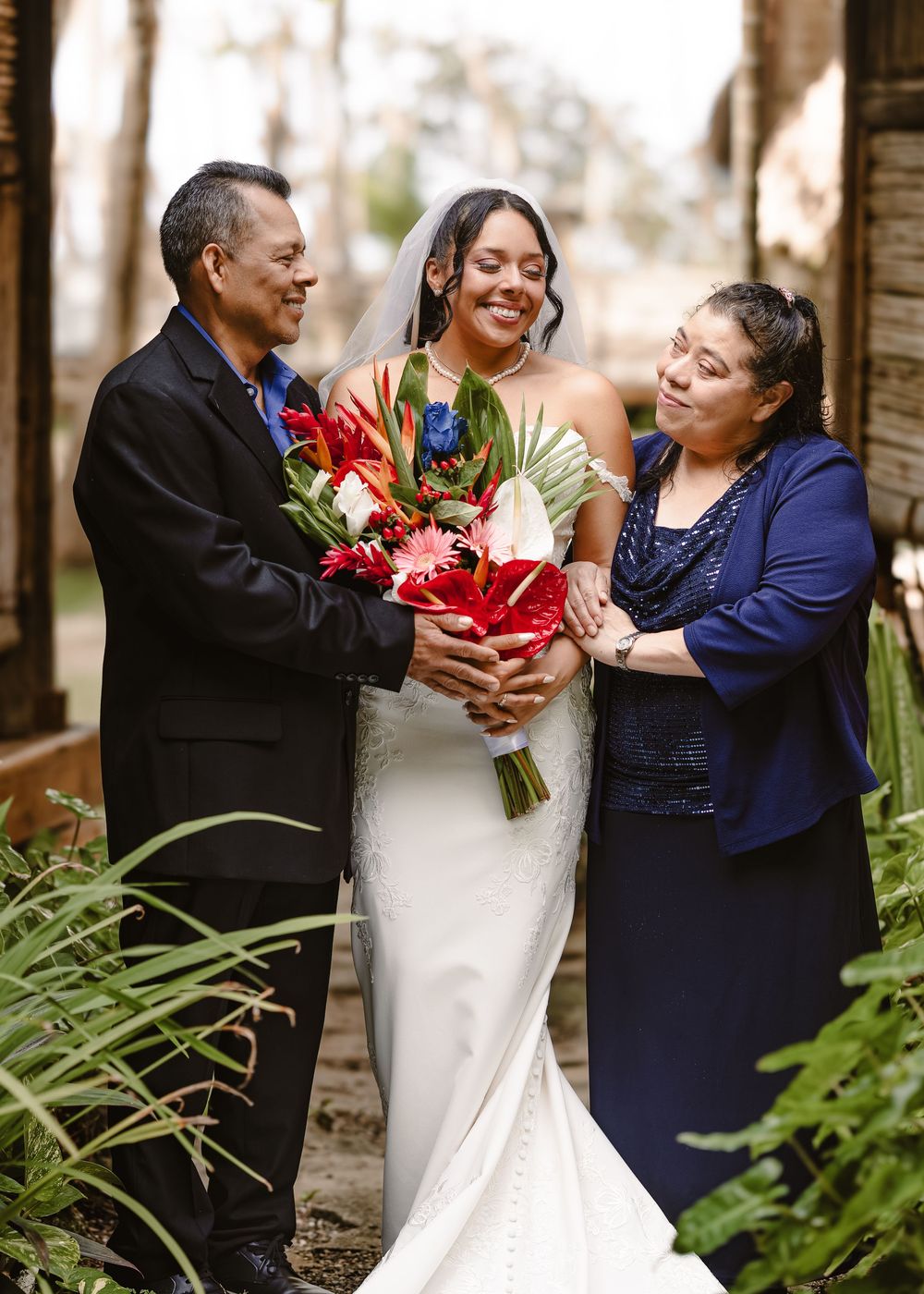 Wedding party poses together outdoors with bride in white dress and family members in formal attire.