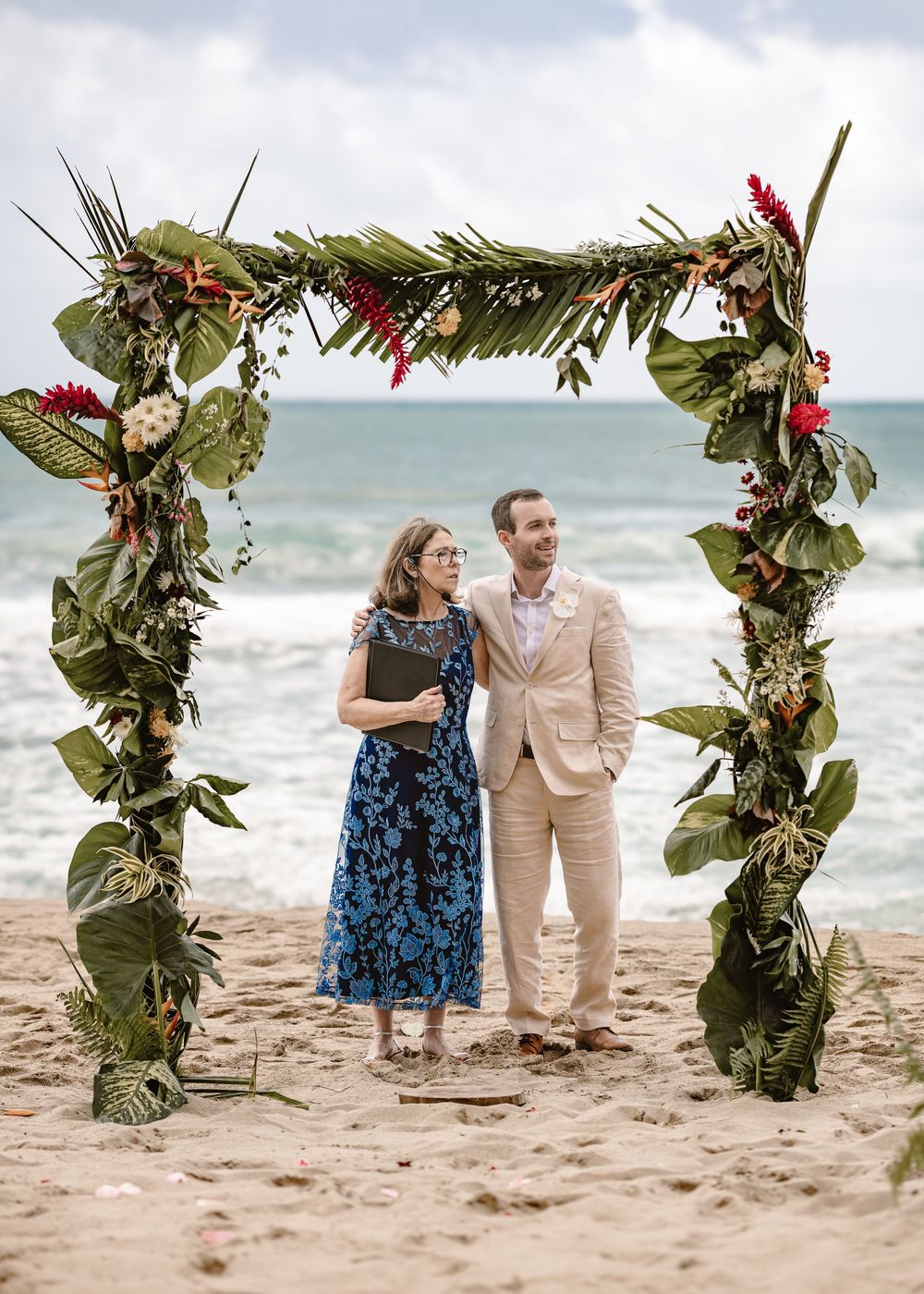 A romantic beach wedding ceremony setup with floral arches and tropical greenery along the sandy shore.