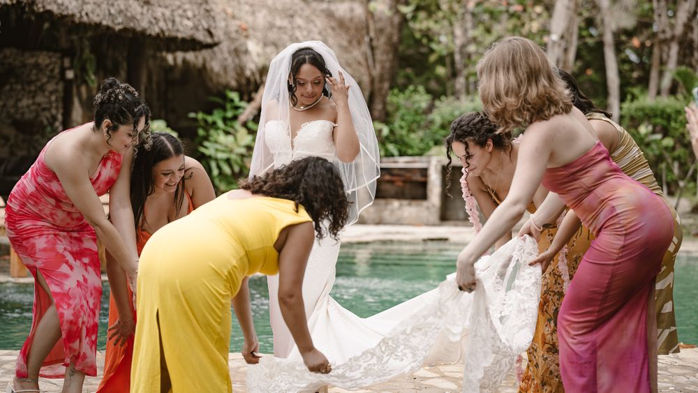 Wedding party helps adjust a bride's dress by a tropical pool.