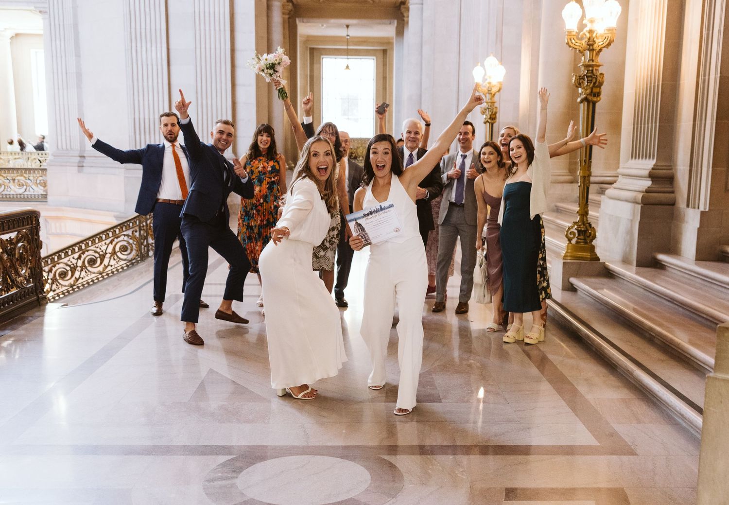 Wedding guests celebrate in an elegant marble hallway with ornate architectural details.