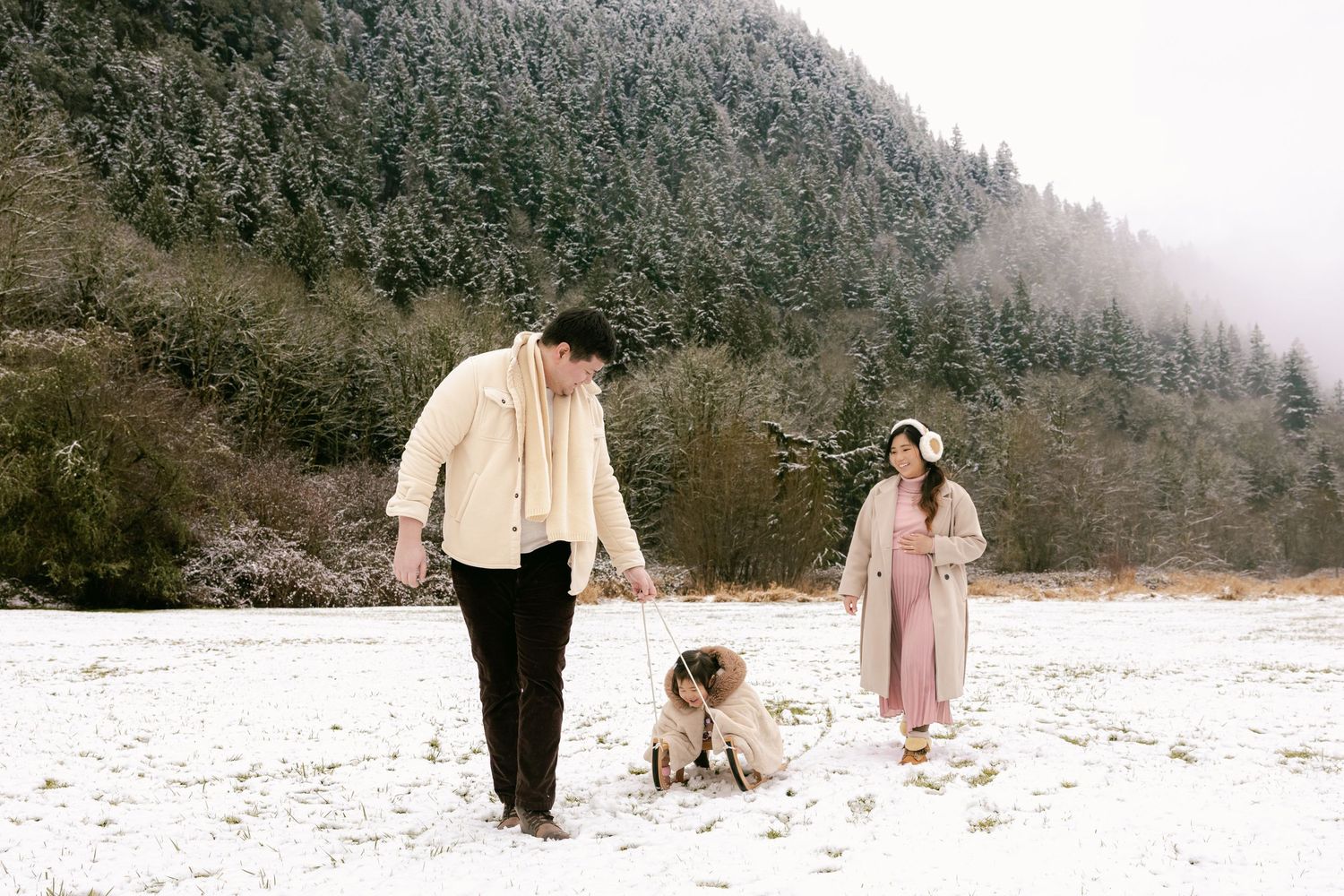 A couple walks through a snowy winter landscape wearing formal attire during an outdoor photo session.