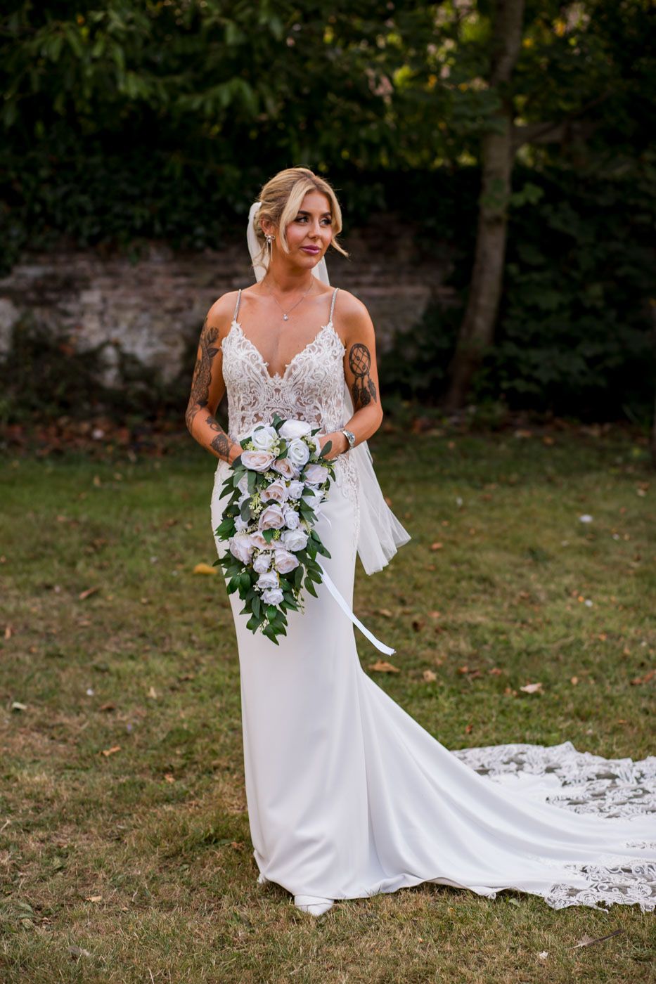 Elegant bridal portrait showing flowing train and floral bouquet against natural backdrop.
