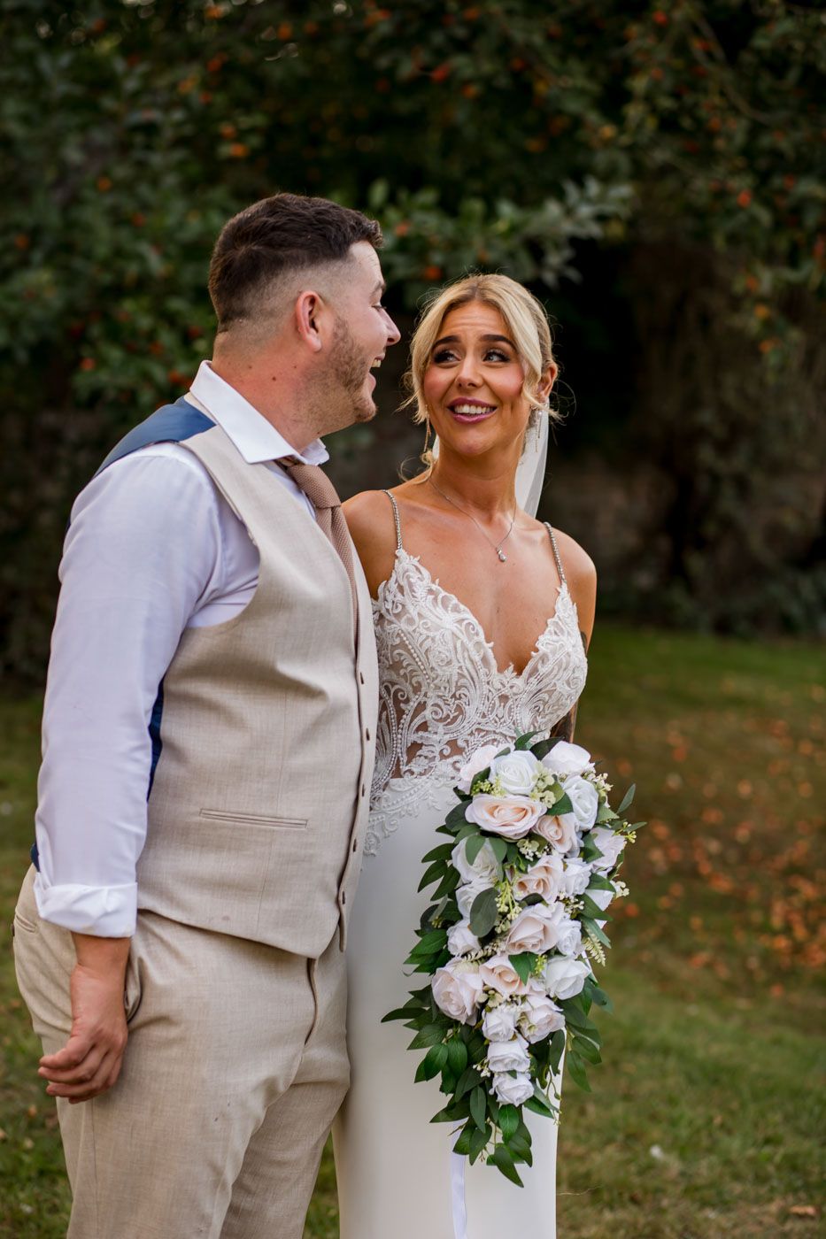 A wedding couple shares an intimate moment while holding a cascading white floral bouquet.