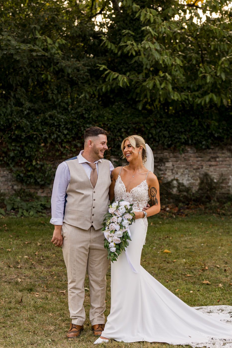 A couple shares a joyful moment in their wedding attire against a garden backdrop.