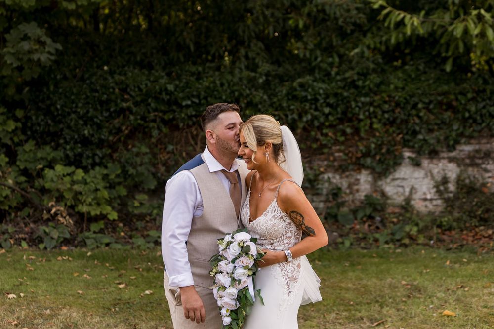 A romantic wedding couple embraces while holding a cascading white orchid bouquet in a garden.