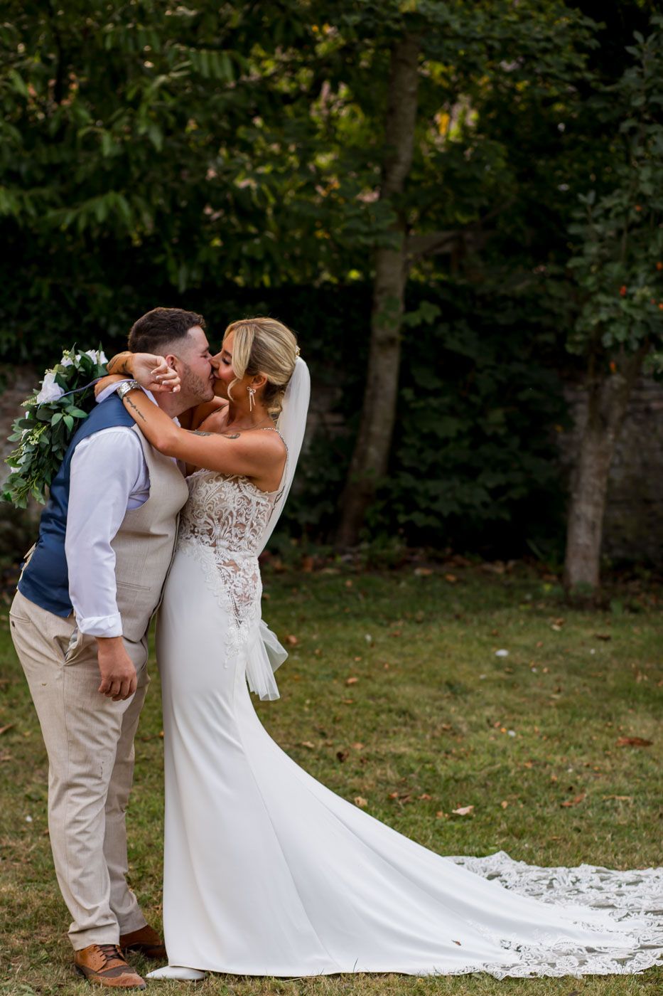 A romantic wedding moment captured in a garden setting with a flowing white lace gown and casual groom attire.