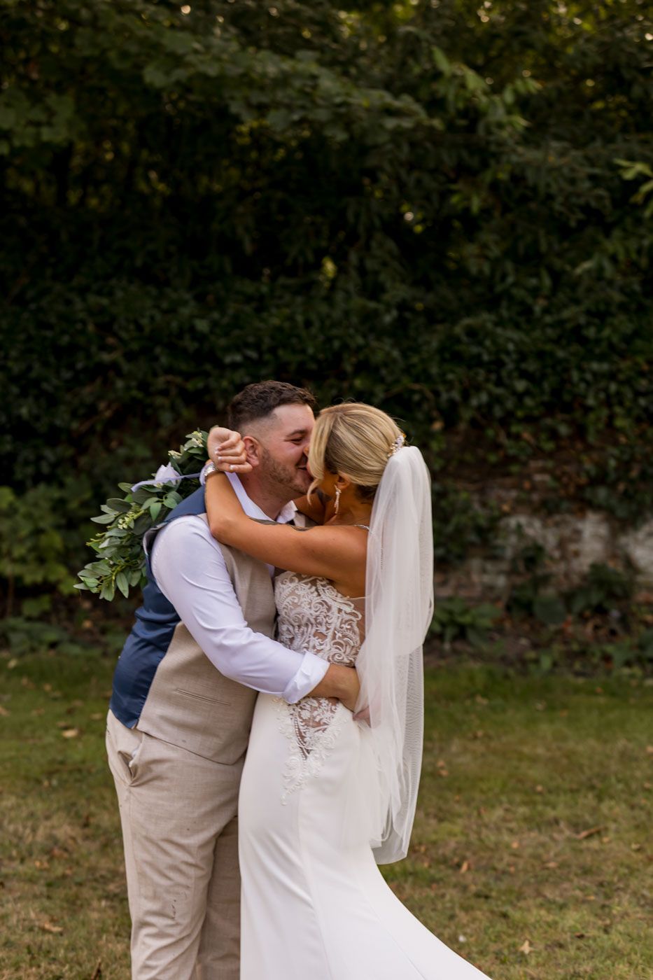 A romantic wedding kiss captured in a garden setting with flowing white dress and veil.