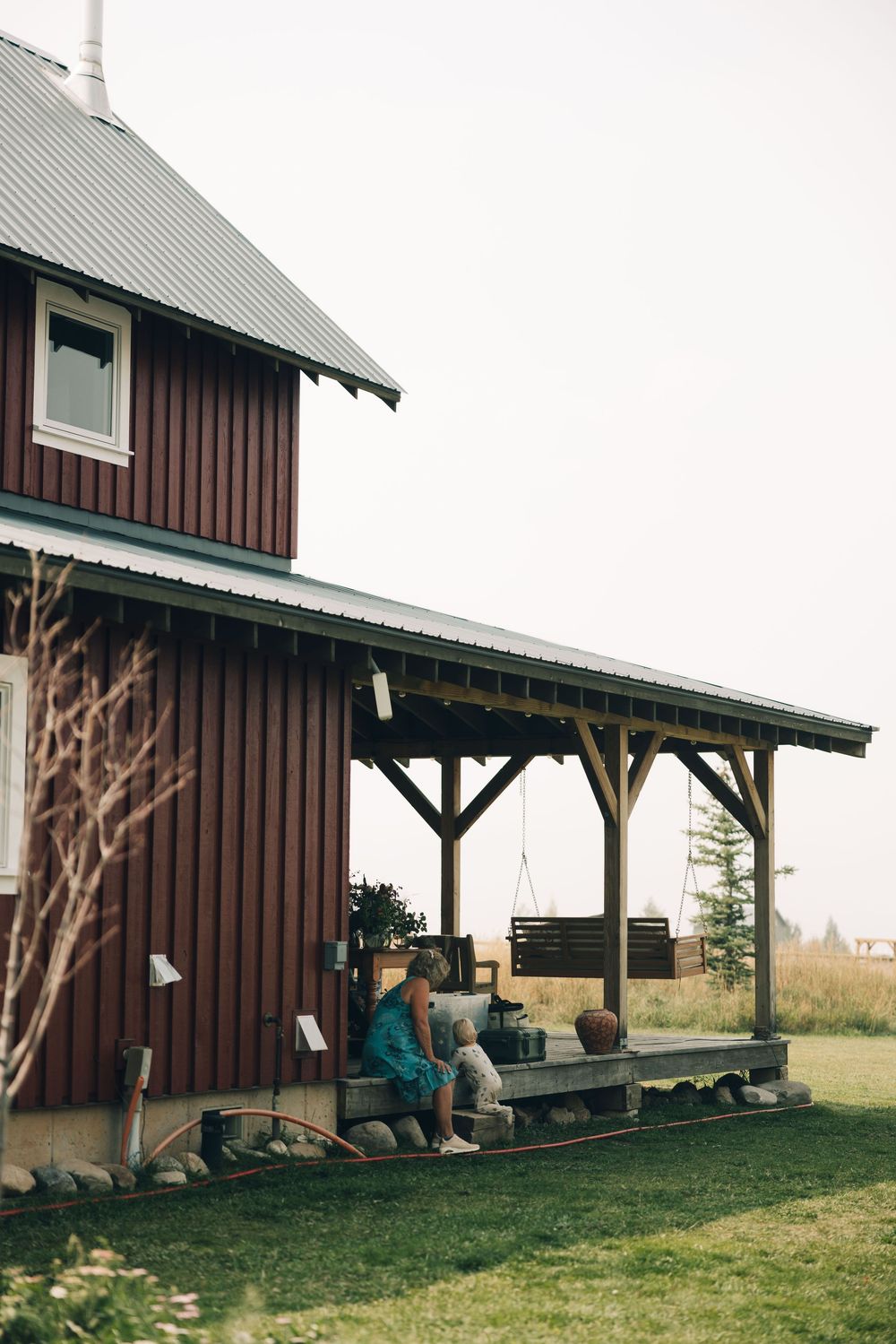 Rustic brown barn with covered porch area surrounded by green grass and countryside views.