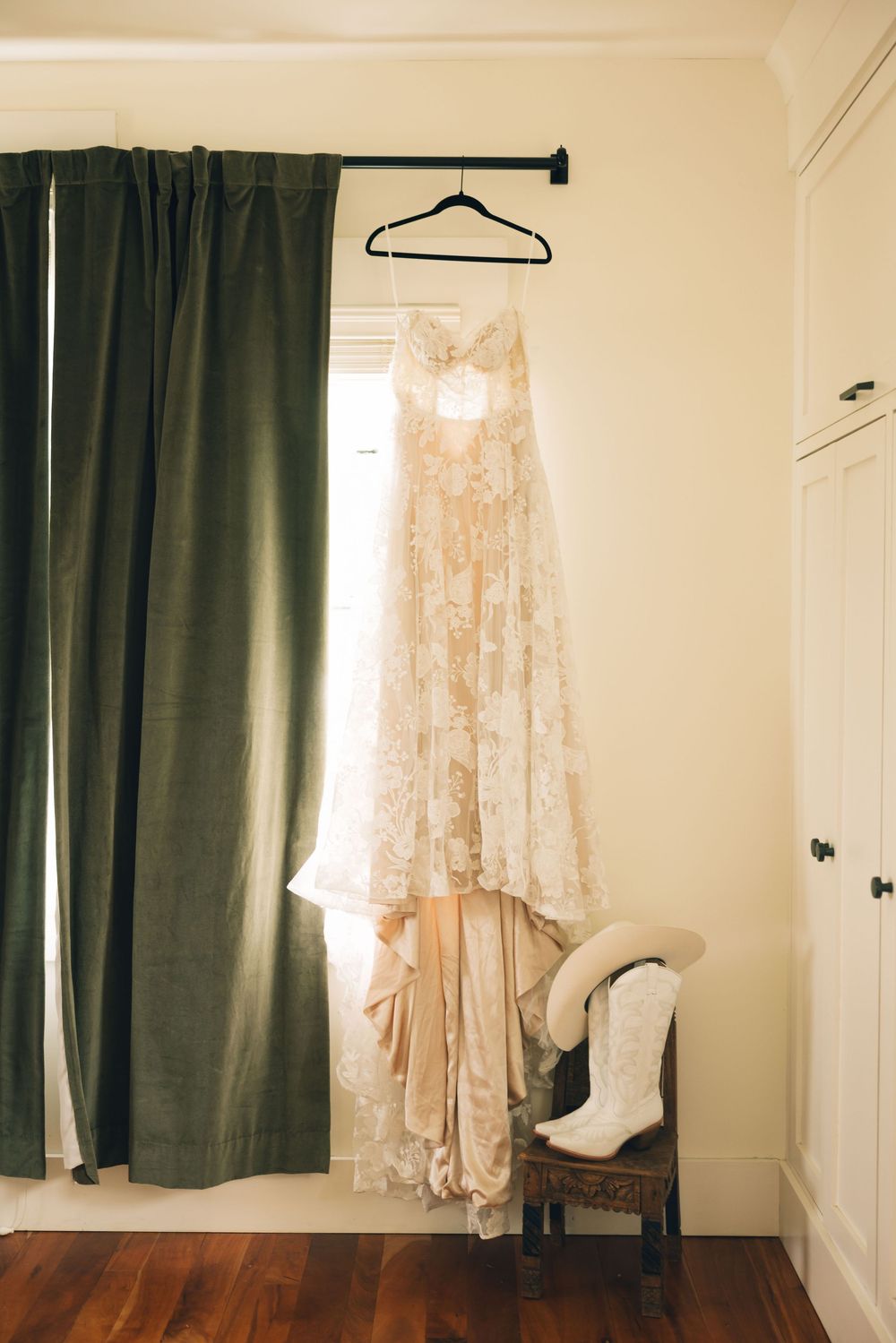 Vintage lace wedding dresses and veils hanging on display against a cream colored wall.