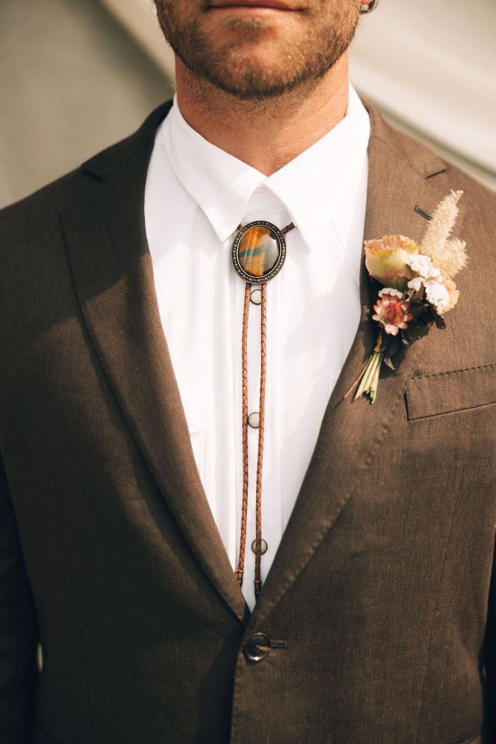 Close-up detail of a brown suit with bolo tie and boutonniere at a western-themed wedding.