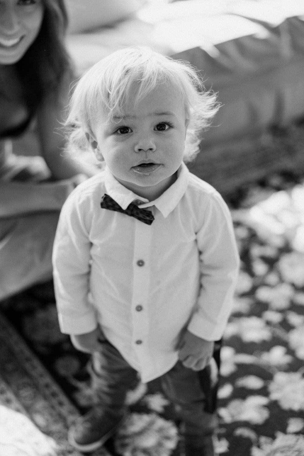 A toddler in a white dress shirt and bowtie smiles at the camera.