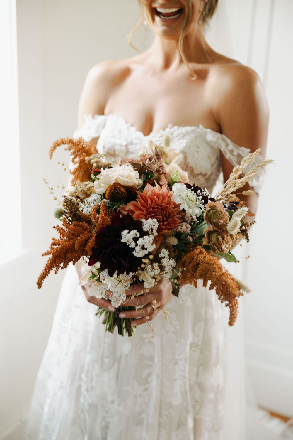 Elegant bridal bouquet featuring rust-colored flowers and white blooms against a white dress.