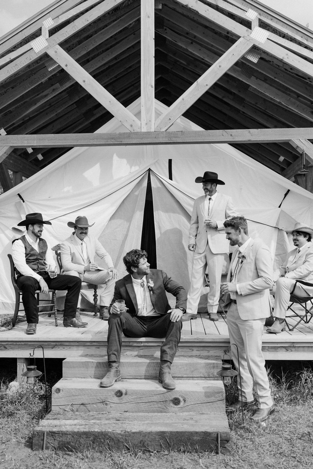 Vintage black and white photo showing cowboys lounging on a wooden porch in casual poses.