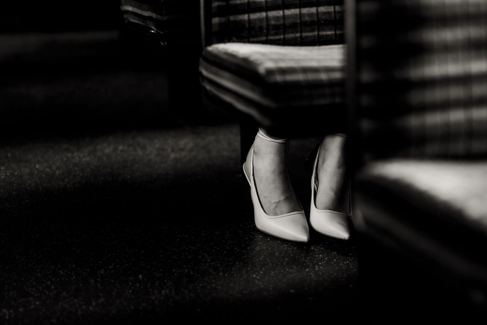 A pair of elegant white high heels photographed in dramatic black and white lighting against a dark floor.