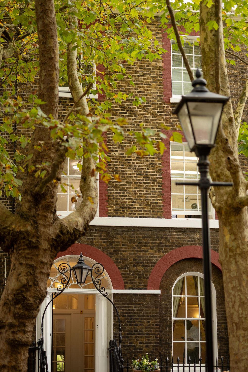 Historic brick building facade with arched windows and vintage lampposts among autumn trees.