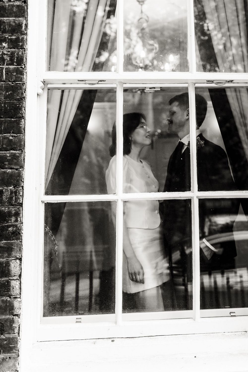 Black and white photograph showing silhouettes through window panes creating a mysterious atmospheric effect.