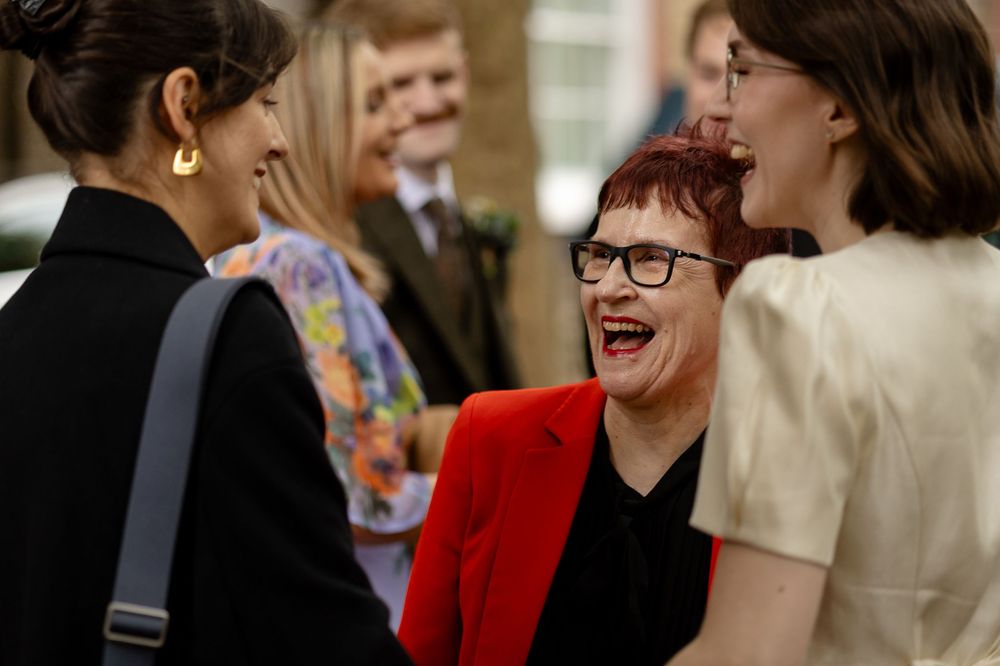 A group of people in formal attire stand together laughing and smiling at an indoor event.