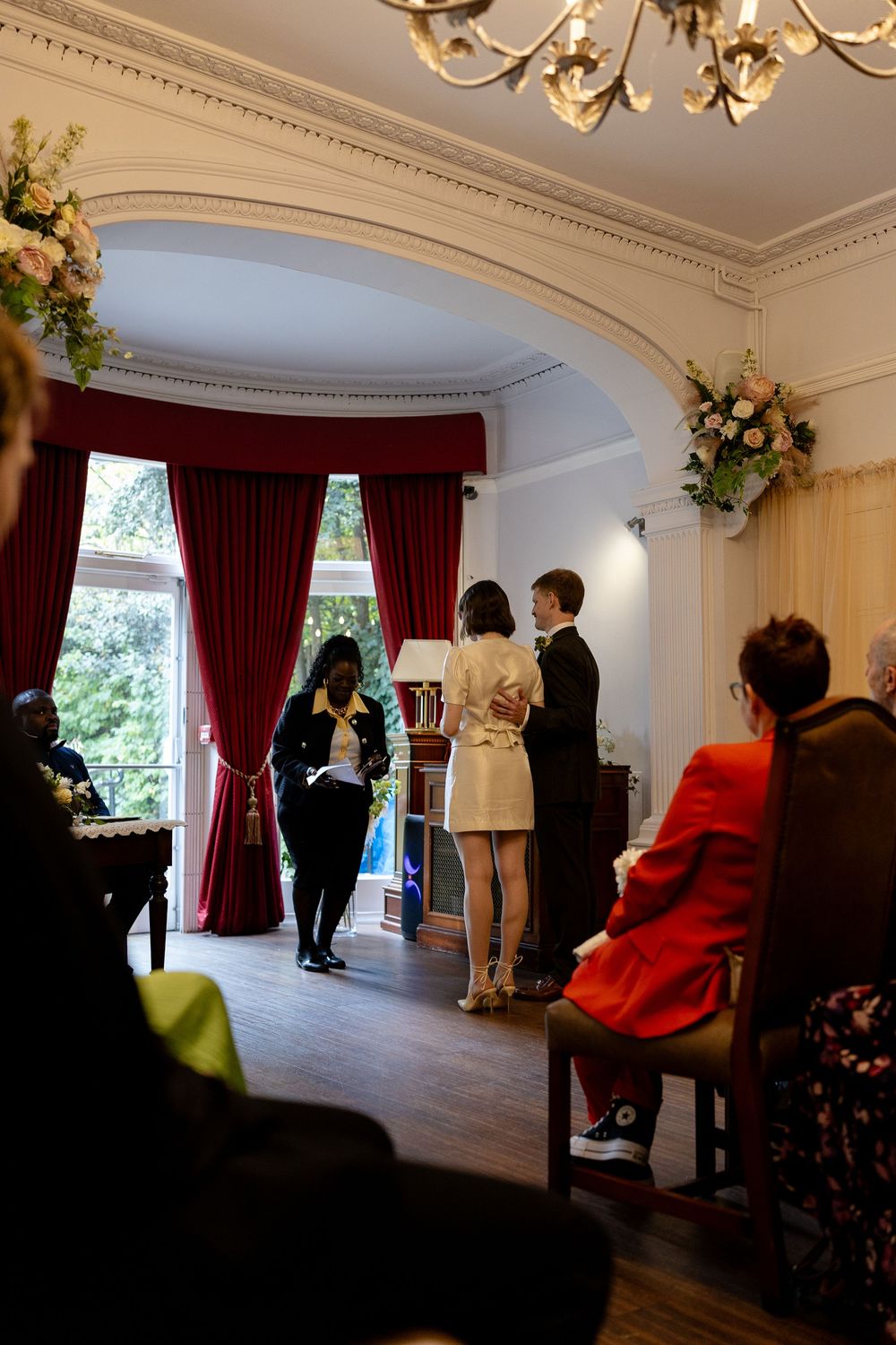 An elegant room with red curtains and ornate molding where people are gathered for an event.