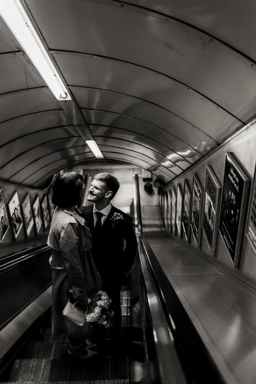 People walking through a curved underground tunnel with fluorescent lighting and reflective walls.