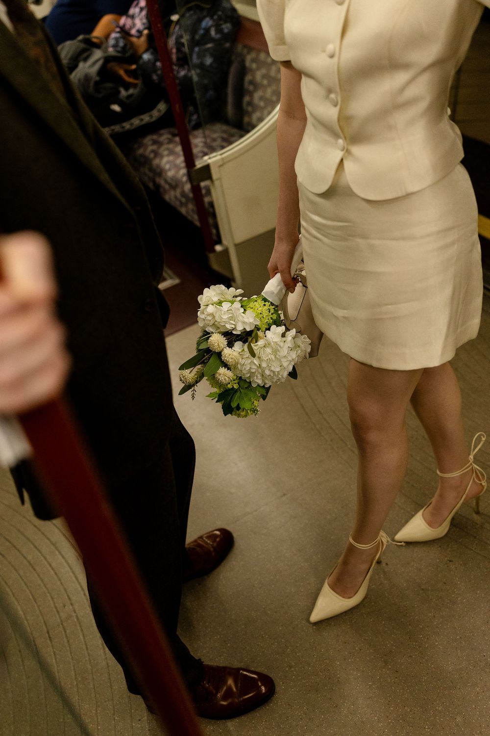 Close-up view of a person wearing a cream-colored dress suit and holding a white floral bouquet.