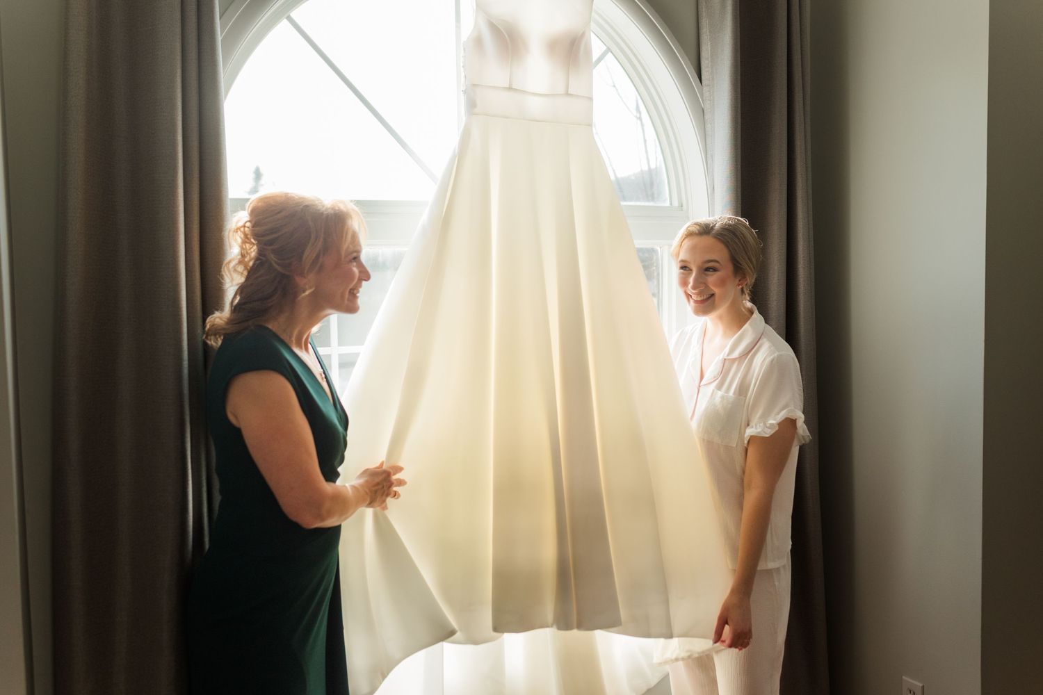 A row of people in white shirts stand in front of sheer curtains in a bright interior space.