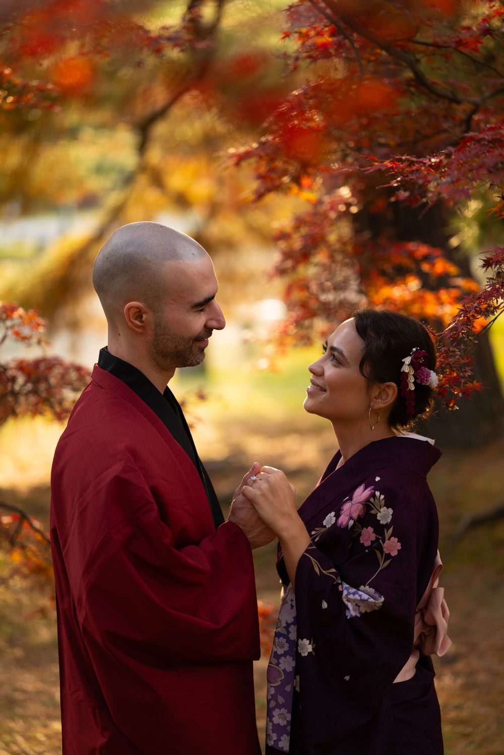 Couple in kimono holding hands and gazing lovingly at each other among colorful fall foliage in Japan.