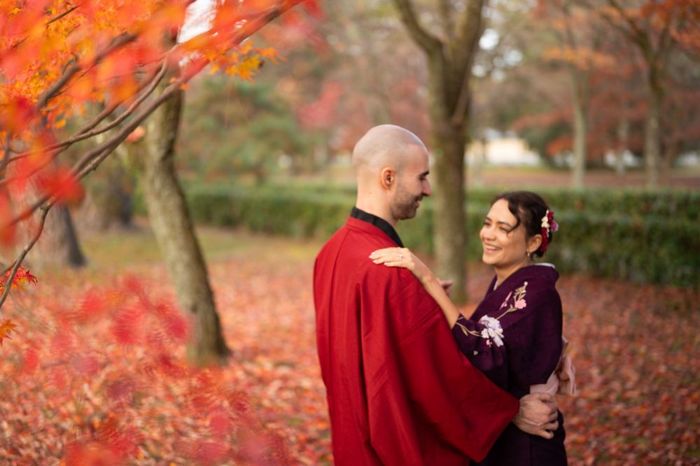 Couple in red and purple kimono sharing a tender moment amid a stunning red autumn leaf landscape.