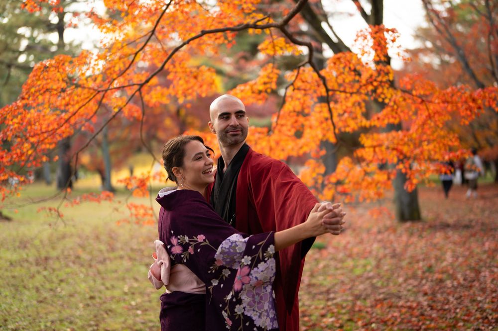Joyful couple in traditional Japanese kimono laughing and embracing under vibrant orange autumn foliage in a park.