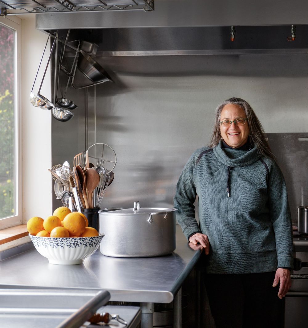 A kitchen interior scene with stainless steel counters, cooking utensils, and a person in a gray sweater.