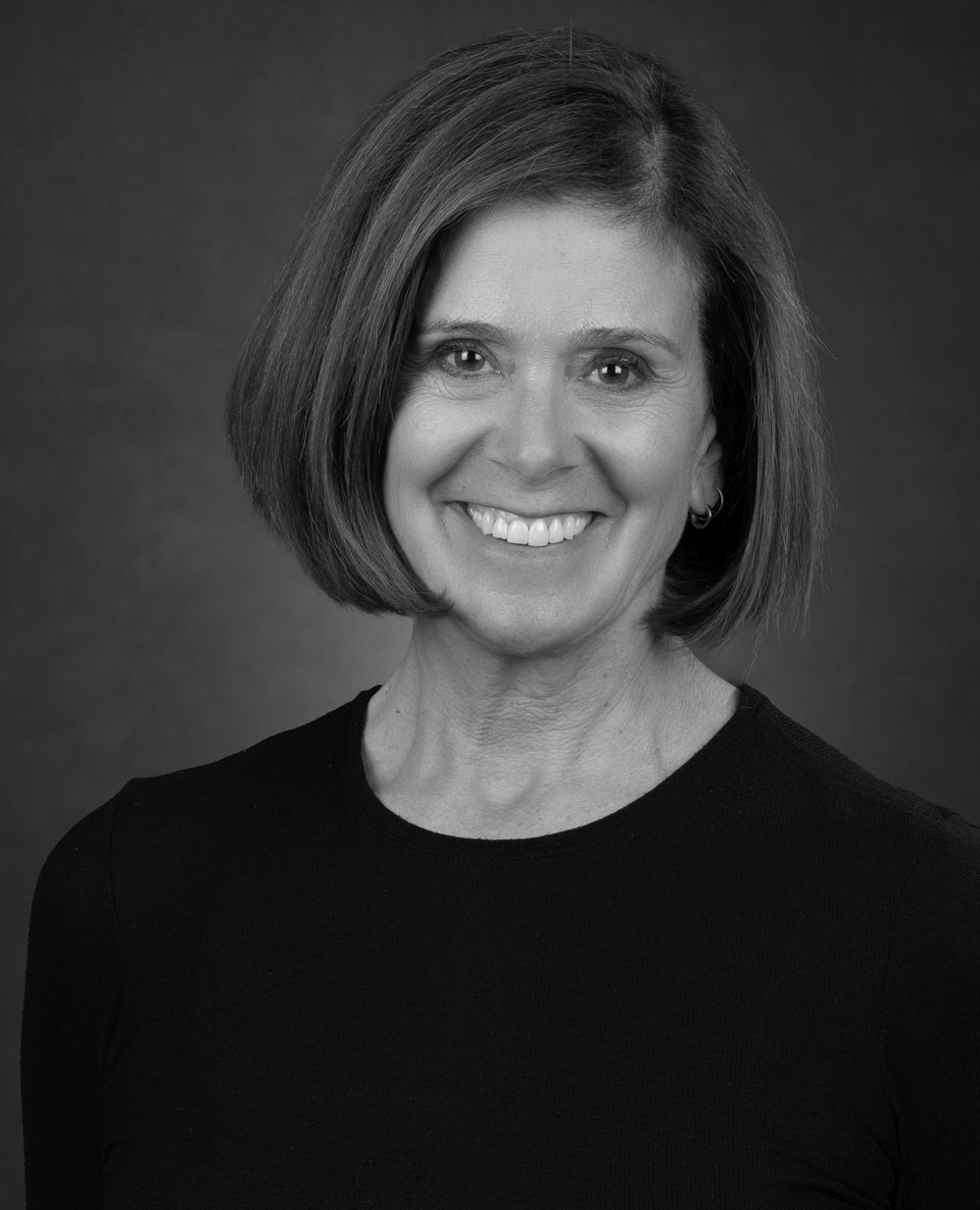 Professional portrait of a person in black attire smiling against a dark background.