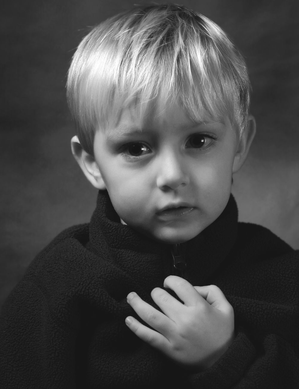 Black and white portrait of young child in dark coat with solemn expression.