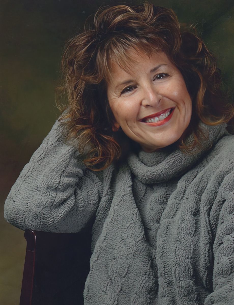 Portrait of mature woman in gray sweater with warm smile and curly brown hair.
