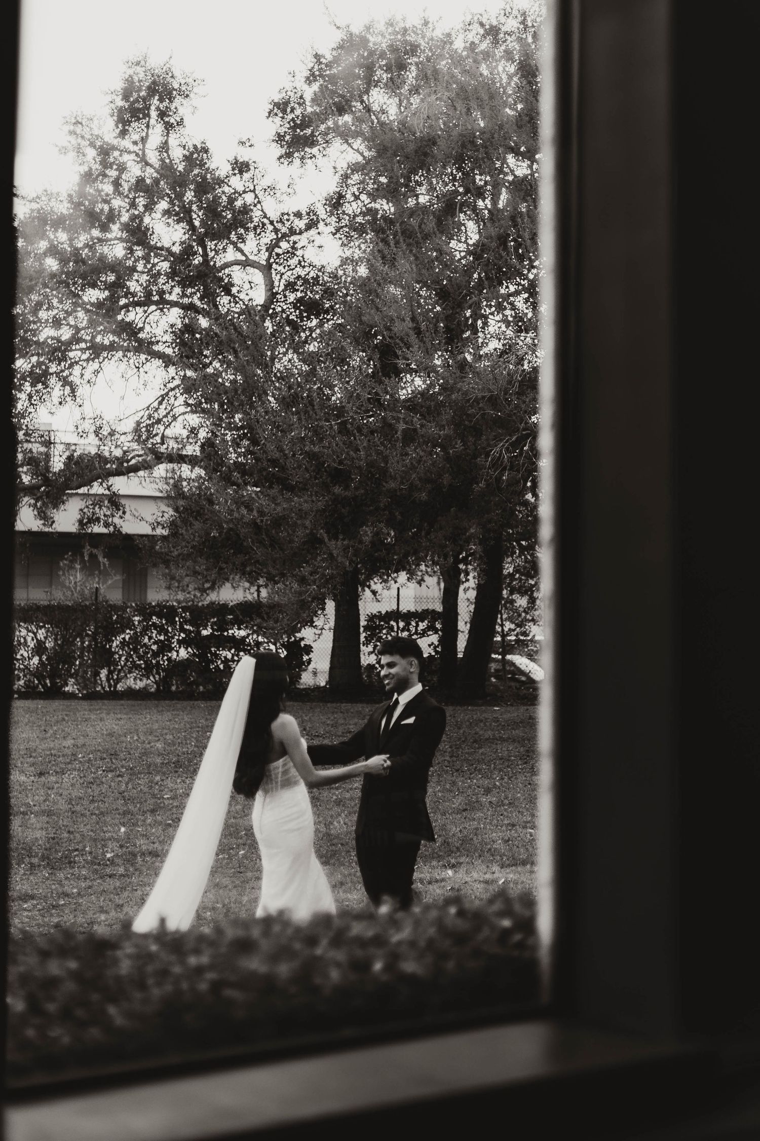 Black and white silhouette of wedding party walking through trees in garden setting.